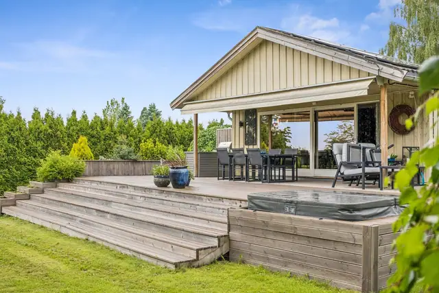 Delvis takoverbygd terrasse med blant annet markise og nedfelt jacuzzi og flotte plantekasser som omkranser terrassen.