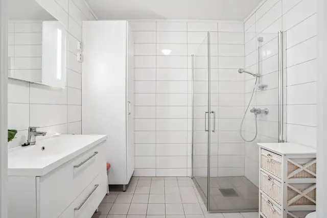 Romslig og pent flislagt bad med varme i gulv. Dusjdører i glass.